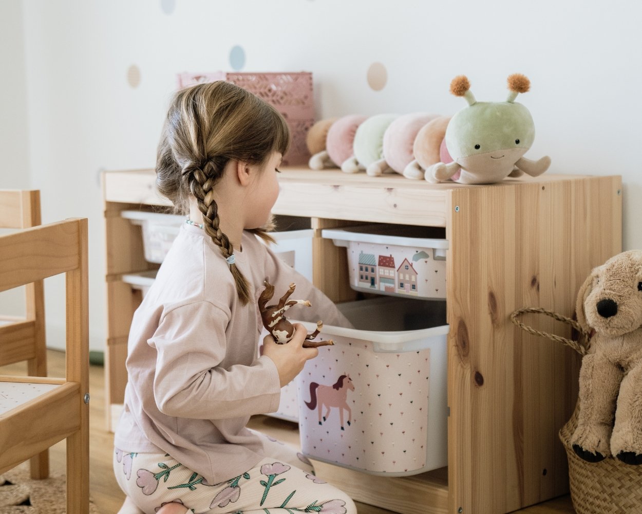 Ein Mädchen spielt in seinem Kinderzimmer Tiere und greift in das Ikea Trofast Regal, welches mit Limmaland Klebefolien mit Pferde Motiven gestaltet wurde