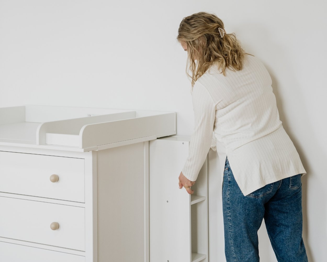 Eine blonde Frau schiebt ein Regal hinter die Wickelkommode von Limmaland